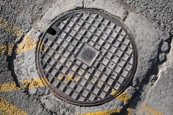 Round metal hatch in urban pavement, sewer manhole cover with yellow road marking lines
