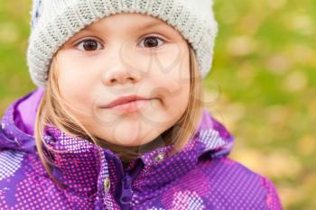 Funny smiling Caucasian little girl, close-up outdoor portrait, walking in autumnal park