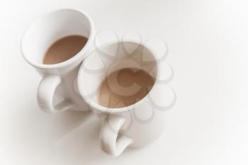 Two big cups full of coffee with milk stand on white table with soft shadow, closeup photo with selective focus