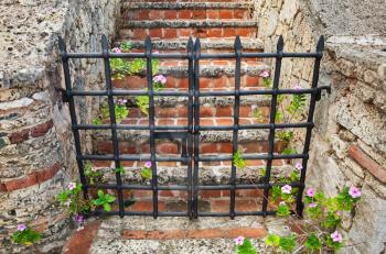Closed black metal gate to the red brick stairway going up