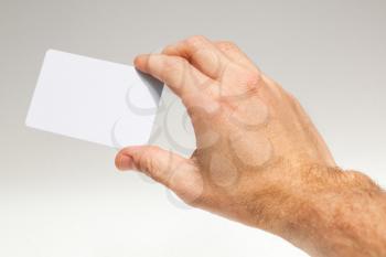 Male hand with white empty card over gray wall background, close up photo with selective focus