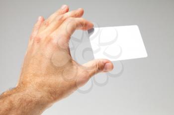 Male hand holds white empty card over gray background, close up photo with selective focus