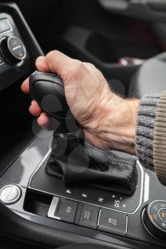 Driver hand holds gear lever of modern luxury crossover car. Closeup photo with selective focus