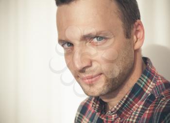 Close-up studio face portrait of young adult European man in colorful casual shirt over white wall with shadow