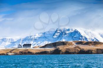 Coastal Icelandic landscape with snowy mountains and small living house under dramatic blue sky. Reykjavik area, Iceland