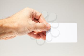 Male hand with white empty card over gray wall background, closeup photo, selective focus