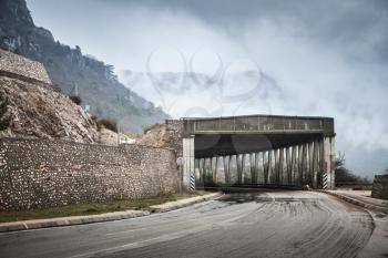 Mountain road with concrete tunnel structure in foggy rainy day, rural auto travel theme