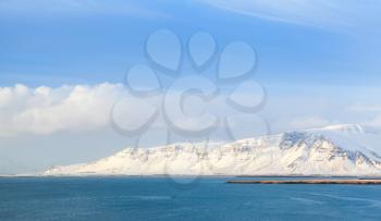 Coastal Icelandic landscape with snowy mountains under blue cloudy sky. Reykjavik distict, Iceland