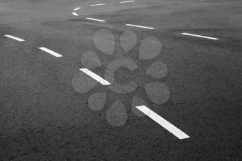 Abstract transportation background. White bent striped dividing lines over dark rough asphalt, road marking. Selective focus with shallow DOF