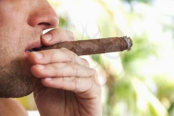Young European man smokes handmade cigar, closeup photo with selective focus. Dominican Republic