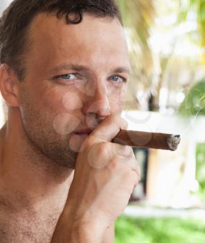 Young European man smokes big cigar, close up portrait with selective focus. Dominican Republic