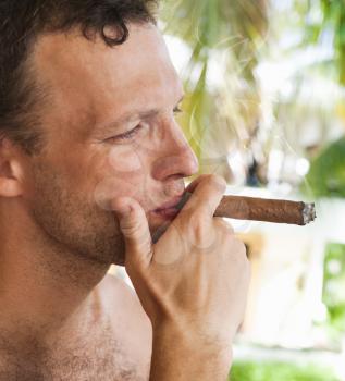 Young European man smokes big cigar, close up profile portrait with selective focus. Dominican Republic