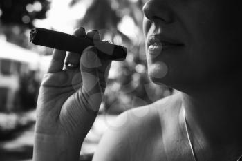 Young European woman smokes handmade cigar, closeup monochrome photo with selective focus. Dominican Republic