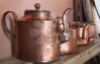 Vintage copper teapots stand on wooden shelf