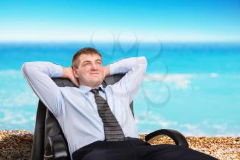 Happy businessman dreaming about vacation sitting in a chair
