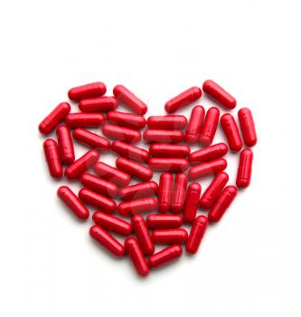 Red long pills in a heart form on white