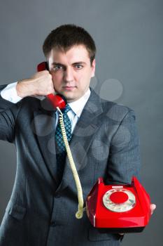 Portrait of a  man  speaking   red phone  isolated on gray background