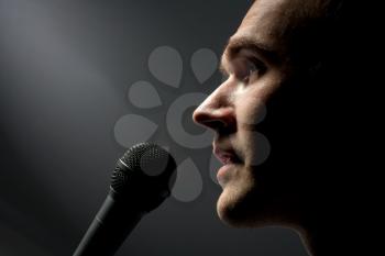 Close-up of man singing to microphone in dark