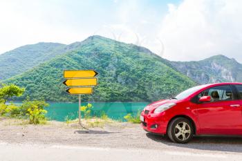 Red car in mountains and road pointer