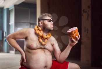 Fat man with sausages round his neck looks at a big wurst in the room