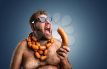 Hungry man with sausages round his neck eats a big wurst over blue