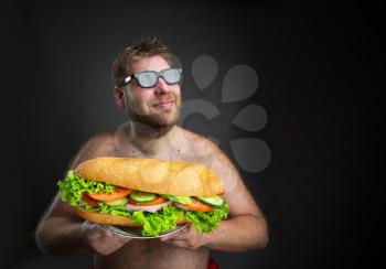 Fat happy man in glasses with sandwich over dark background