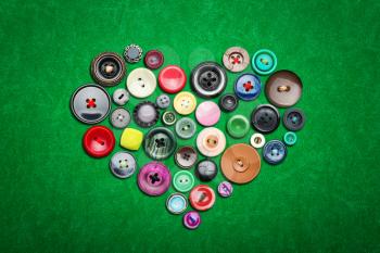 Many colorful buttons in heart shape on green cloth