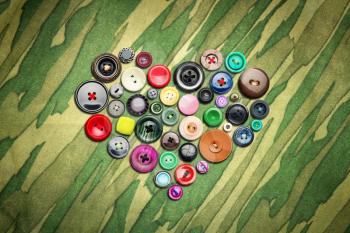 Many colorful buttons in heart shape on khaki cloth