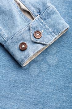 Sleeve of jean cardigan with two plastic buttons against jeans 
