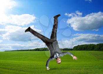 Businessman standing on one hand in summer meadow