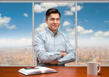 Young businessman sitting at the wooden table smiles in the office