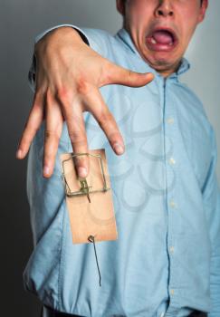 Businessman's finger catched in the mousetrap over grey