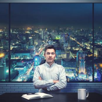 Young businessman sitting in the office against night city