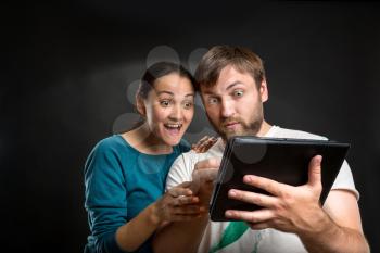 Excited couple watch something on the tablet over black background