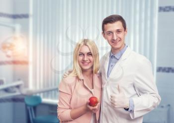 Happy woman stands with a dentist and holds an apple