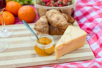 Side view of different products on the blanket served for picnic: cheese, honey and croissants