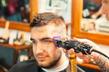 Side view of a young man having hair dress, barber working with hair clipper