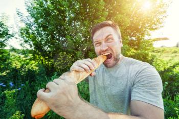 Bearded man nibbling French bread on nature