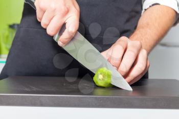 Close up of man's hands slicing kiwi fruit on the board