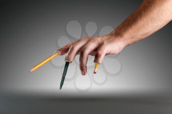 Male hand with pen and pencils instead of fingers over grey