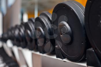 Heap of black dumbbells with weight plates on the rack