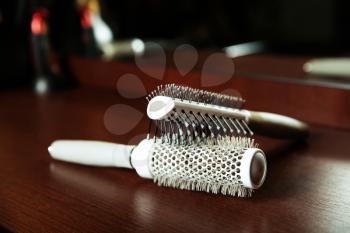 Hairbrushes are located on a wooden table, hairdressing tools on the background.
