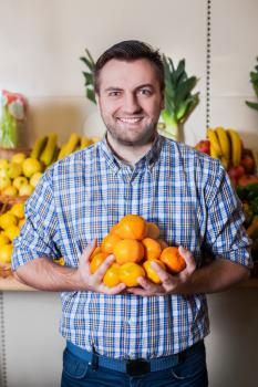 Portrait of smiling man holds ripe tangerines in hands.
