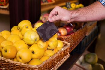 Mans hand holds price tag on ripe apples in grocery. Ecological food. Yellow apples in a box.