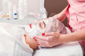 Beautician apply facial cream on young woman face skin. Cosmetic procedure in spa salon. Mask for facial skin care