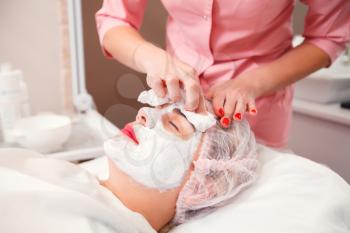 Beautician apply facial cream on young woman face skin. Cosmetic procedure in spa salon