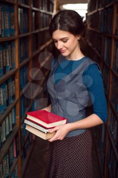 Student girl or woman with books between bookshelves in library.