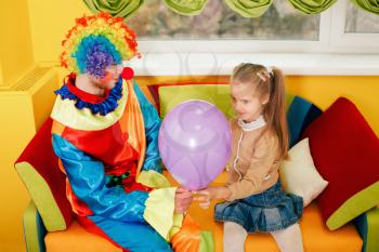 Amusing clown give air balloon to the little girl. Clown in colorful costume on birthday party.