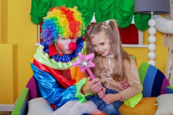 Little girl playing with cheerful clown in funny costume. Friendship concept