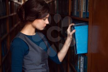 Young woman taking book from library shelf. Knowledge, education and studying concept.